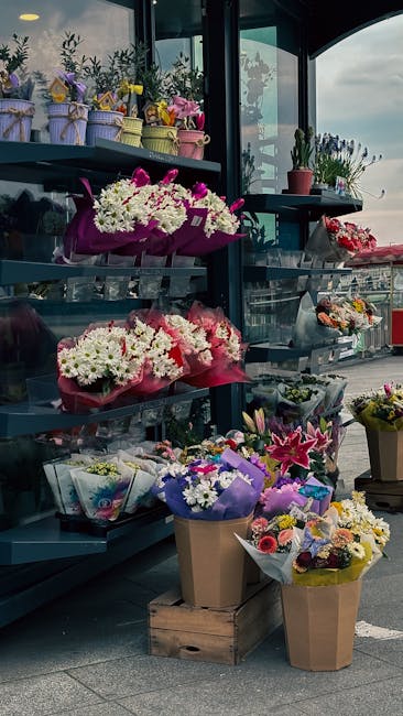 A display of various floral arrangements and bouquets at a flower shop, featuring a range of fresh flowers in vibrant colors including white, pink, purple, and yellow. The flowers are arranged in pape